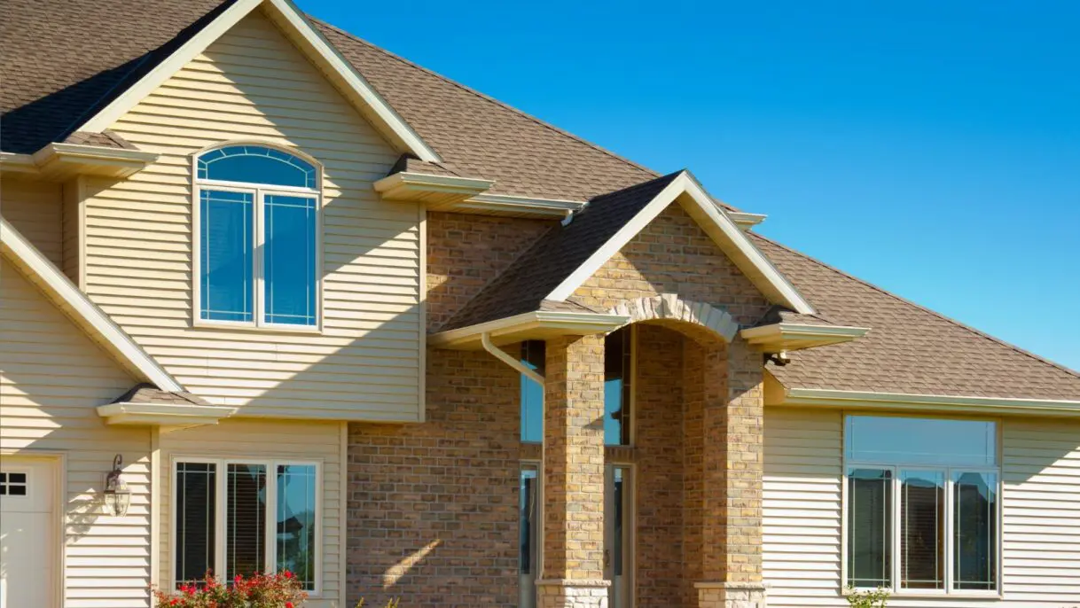 Modern two-story home with mixed brick and vinyl siding, asphalt shingle roof, arched windows, and well-maintained exterior trim under clear blue sky
