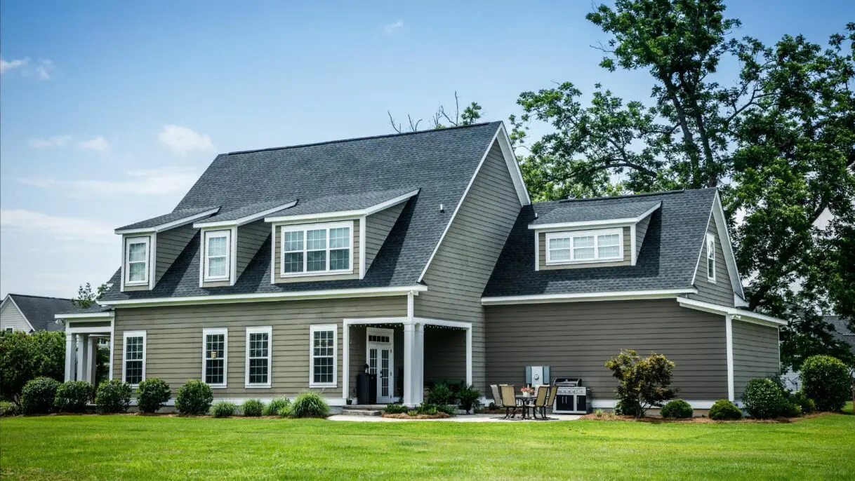 Modern two-story colonial home with gray vinyl siding, white trim, dual dormers, asphalt shingle roof, front porch, and manicured lawn