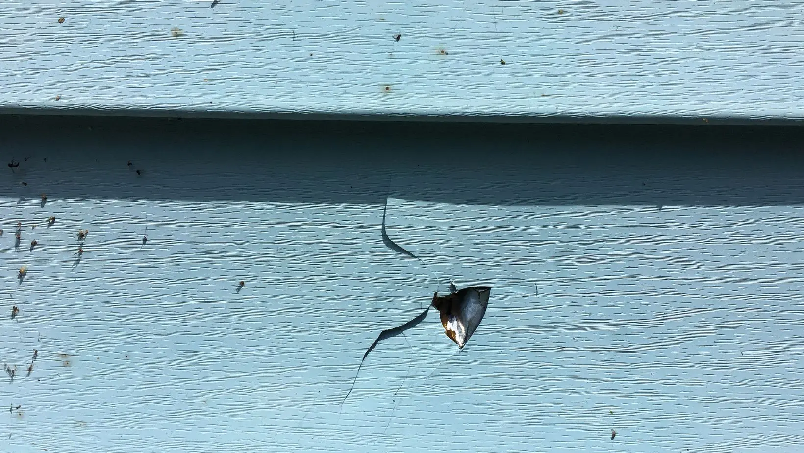 Close-up of damaged blue vinyl siding with a large crack and hole, exposing the material underneath. Signs of wear, impact damage, or weather-related deterioration. Empire Contractors offers expert siding repair and replacement to restore home exteriors.