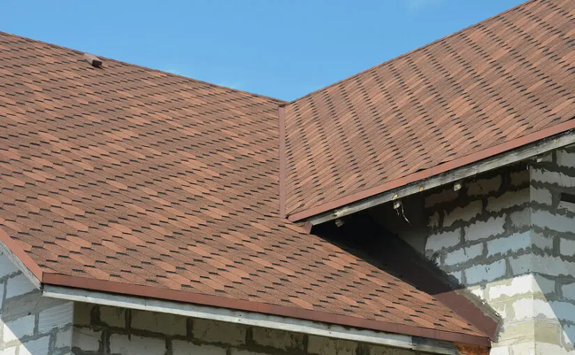 Asphalt shingle roof with valley and ventilation vent against brick chimney under clear sky