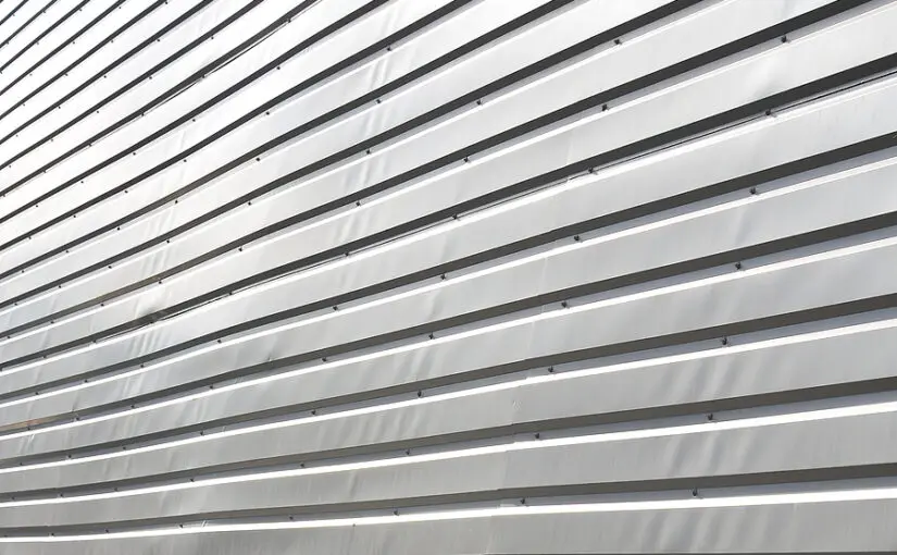 Horizontal metal siding with aluminum plates and relief texture, showing commercial or industrial exterior cladding installation