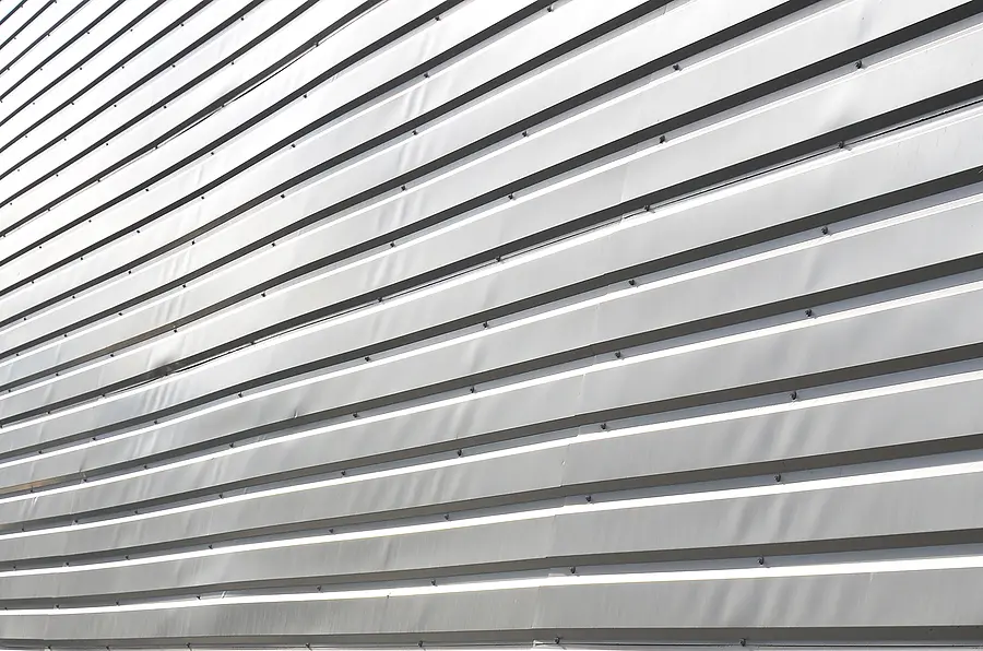Horizontal metal siding with aluminum plates and relief texture, showing commercial or industrial exterior cladding installation