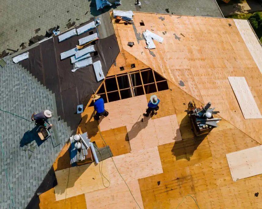 Aerial view of roofers installing plywood sheathing and underlayment during roof replacement, with materials and safety equipment visible on the work site