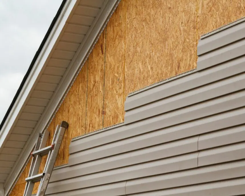 Exterior home showing metal ladder against OSB sheathing and beige vinyl siding installation on residential house