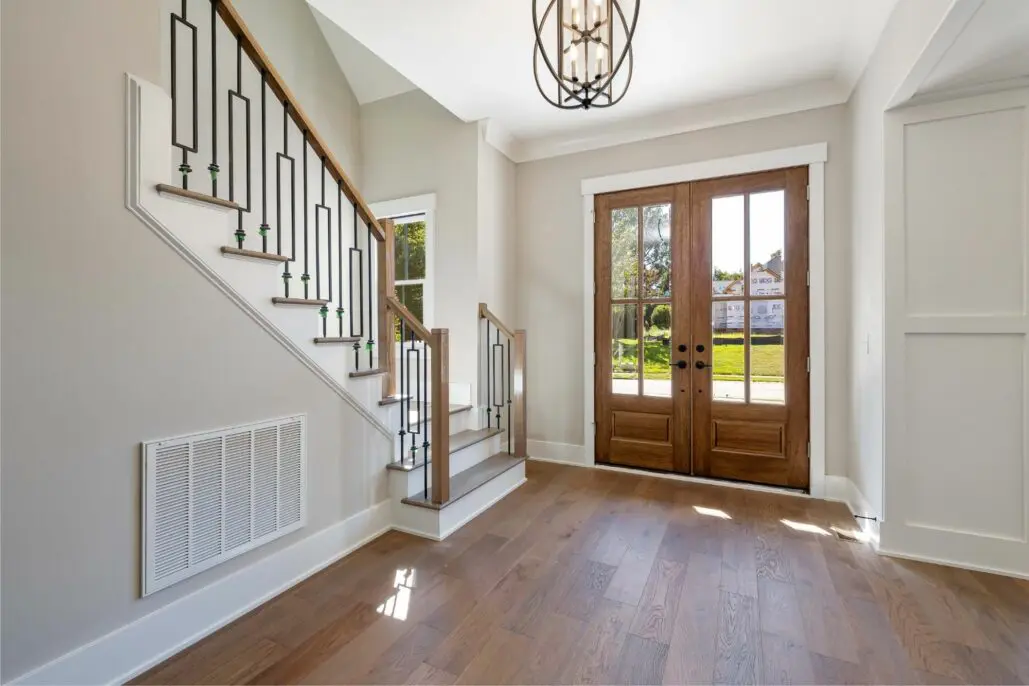 Bright foyer with wooden double French doors, wooden staircase with black metal railing, hardwood flooring, and large window overlooking green lawn