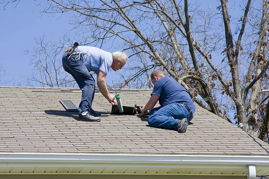 Two roofers inspecting and repairing asphalt shingle roof damage on residential home during roof inspection and repair assessment