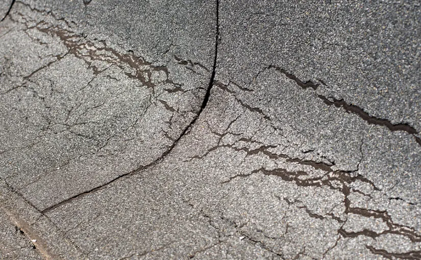 Cracked and deteriorated asphalt shingle roof with storm damage and missing sections exposing underlying layers