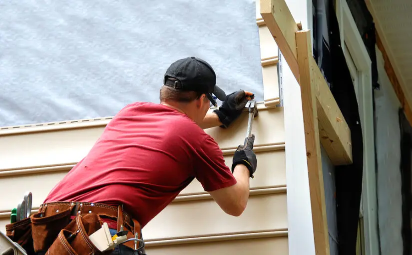 Worker in red shirt installing vinyl siding on house exterior wall during home repair project