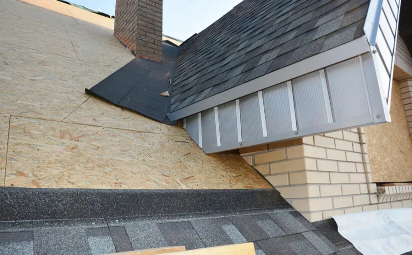 Asphalt shingle roof corner construction showing flashing installation, chimney flashing, and house wrap on brick and siding exterior during roof repair