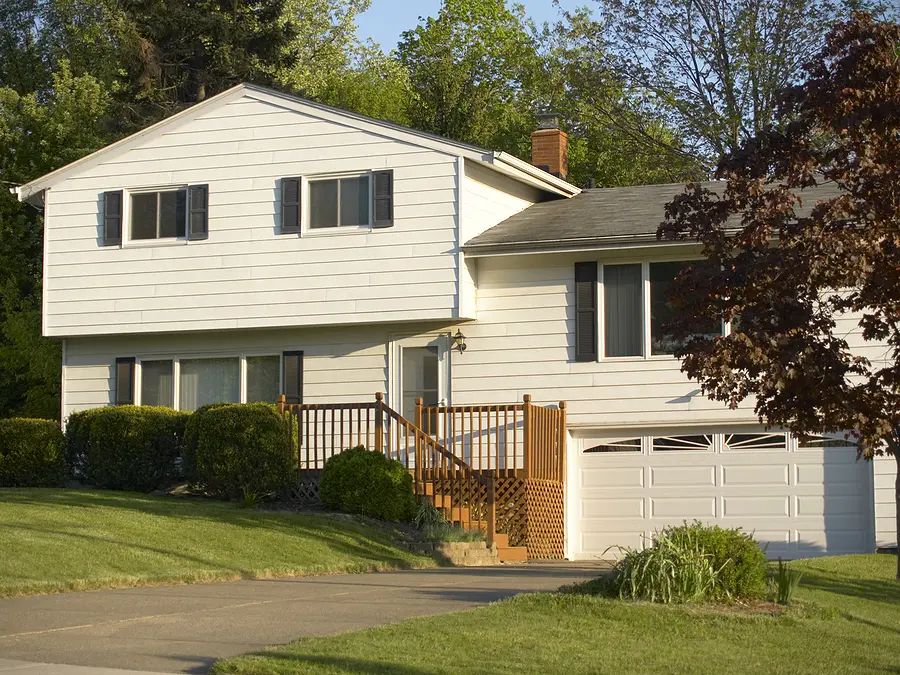 White split-level home with asphalt shingle roof, vinyl siding, wooden deck, attached garage, and mature landscaping in Cincinnati Ohio residential area