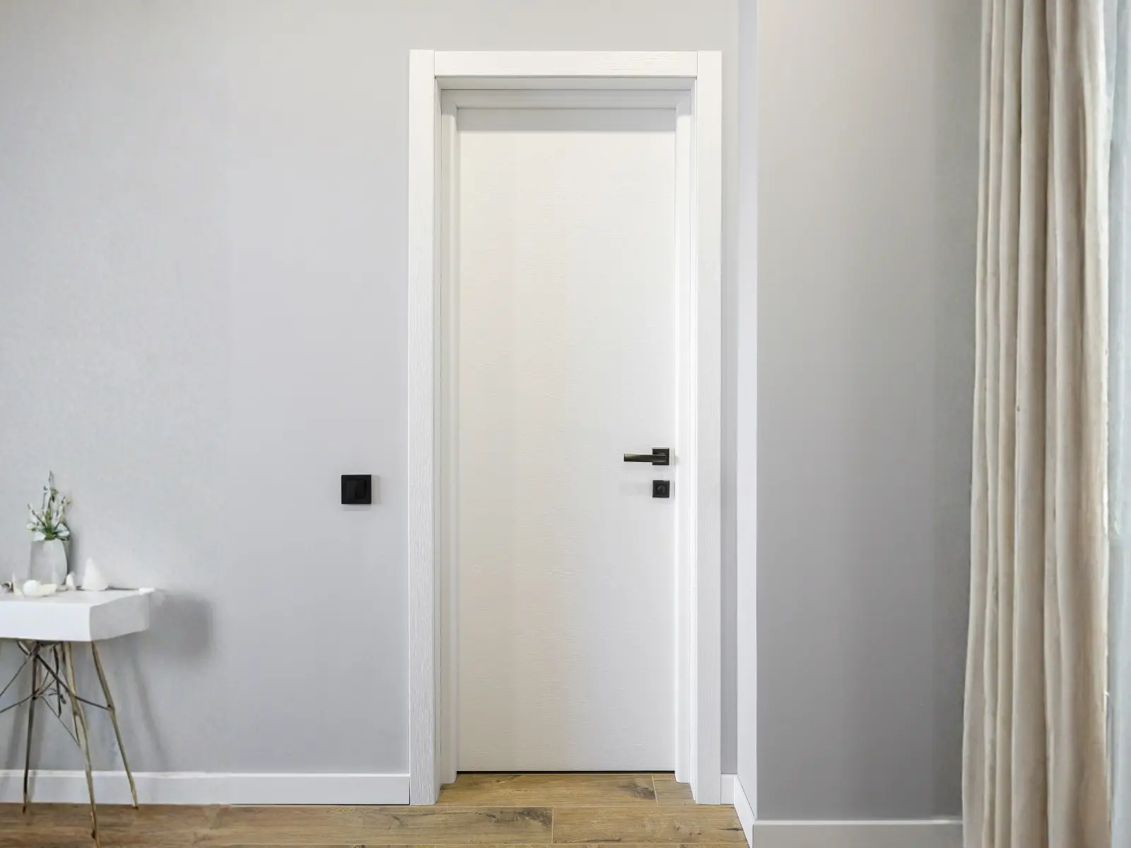 Modern minimalist hallway with white interior door featuring black hardware and white trim frame