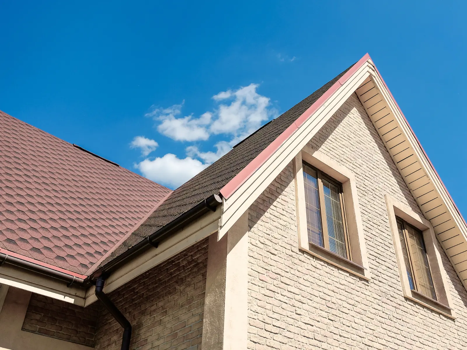 Residential home exterior showing brick and vinyl siding with a peaked gable roof and asphalt shingle roofing against blue sky
