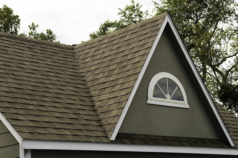Residential house with peaked roof covered in asphalt shingles, featuring a semicircular window in the dark gray gable and white trim along the roofline