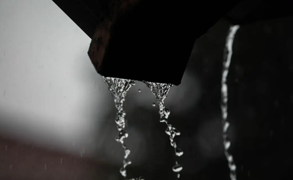 Close-up of rainwater flowing from gutters, showing water dripping off the edge during a heavy rainstorm.