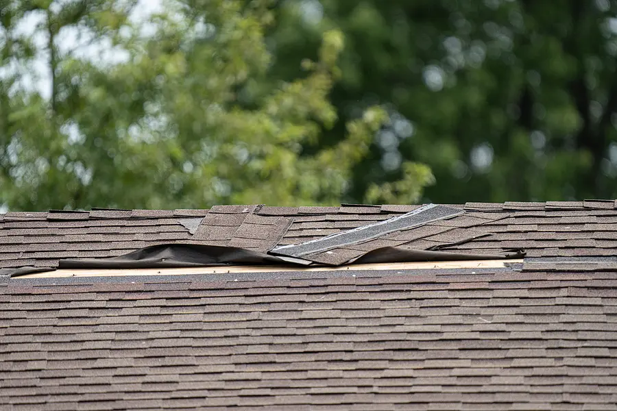 Damaged asphalt shingle roof with missing and lifted shingles from storm and wind damage, showing need for roof repair or replacement