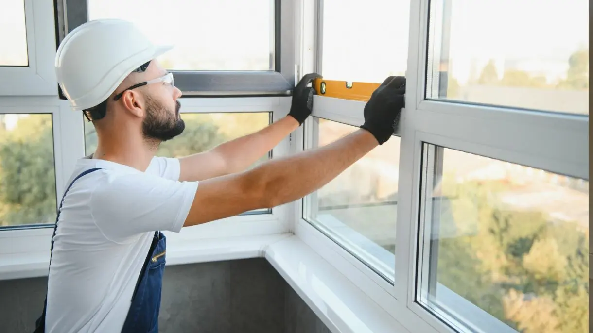 Contractor in hard hat and safety glasses installing level on window frame during home exterior renovation