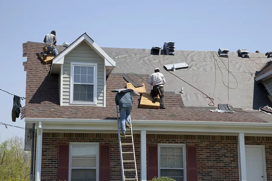 Roofers installing asphalt shingles on residential roof with missing shingles and storm damage visible on brick home in Cincinnati Ohio