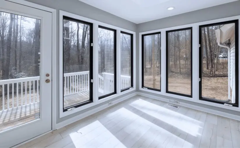 Bright sunroom with multiple black-framed glass doors and windows overlooking bare winter trees and wooden deck