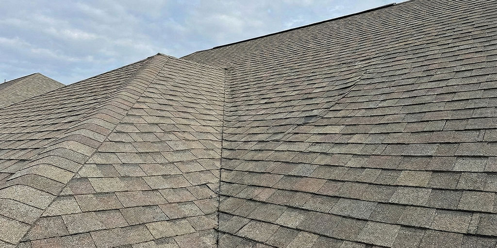 Close-up view of an asphalt shingle roof showing uneven lines and minor buckling, indicating potential structural or ventilation issues.