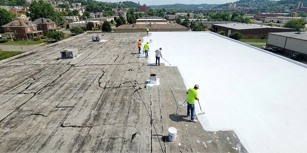 A crew applying a white silicone roof coating to a commercial building.